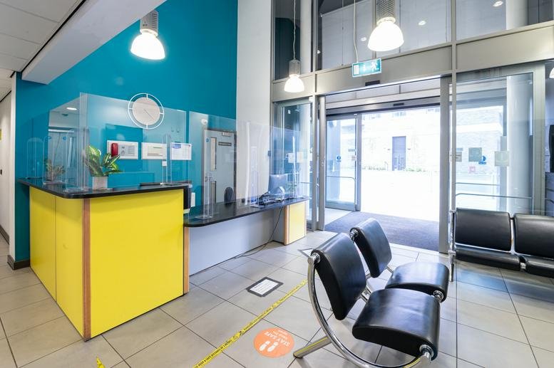 Modern reception area at 50 Cambridge Road, Barking with a bright yellow desk and bold teal feature wall.