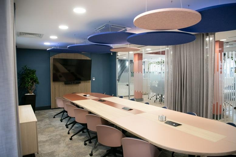 Meeting room at 55 St Paul's Street with a long oval table, pink chairs, and blue acoustic ceiling panels.