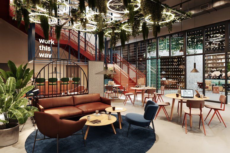 Spacious communal lounge with leather seating, hanging plants, and a red industrial staircase.