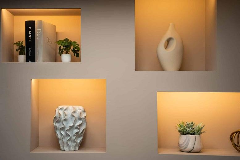 Modern wall niches with warm backlighting displaying books and decorative vases.