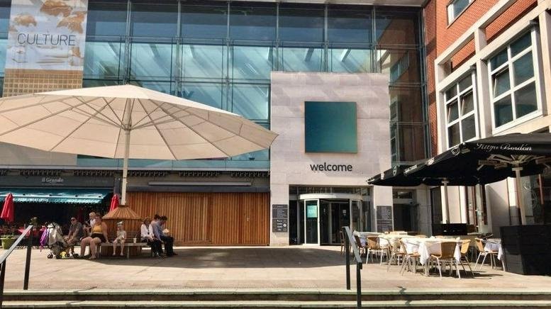 Exterior entrance of 6-7 Derby Square, Epsom with a large patio umbrella and cafe seating.