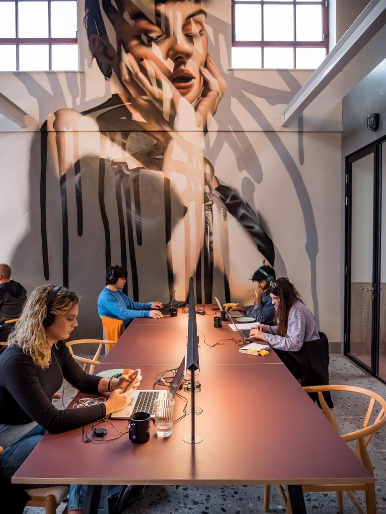 Spacious communal area at 64 Jersey St, Ancoats featuring a large mural and long shared work table.