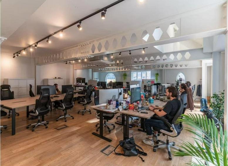 Open-plan office with wooden floors, track lighting, and indoor plants.