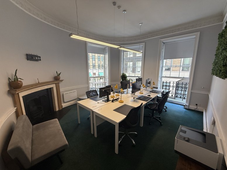 Coworking space showing a lounge area with a fireplace and desks near large windows.