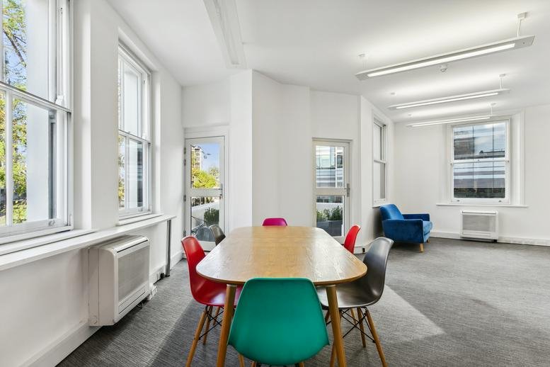 Communal breakout area at 7, Lyric Square, London with colorful chairs and a long wooden table.