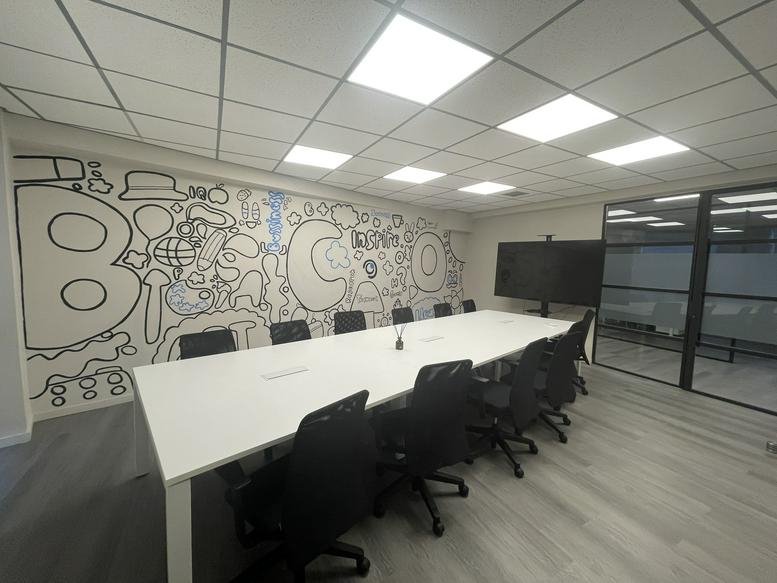 Meeting room with a white conference table, black chairs, and a creative wall mural.