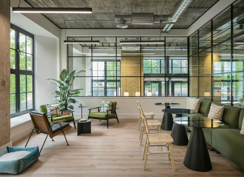 Spacious communal lounge at Riley Studios with industrial ceilings, green velvet seating, and large windows.