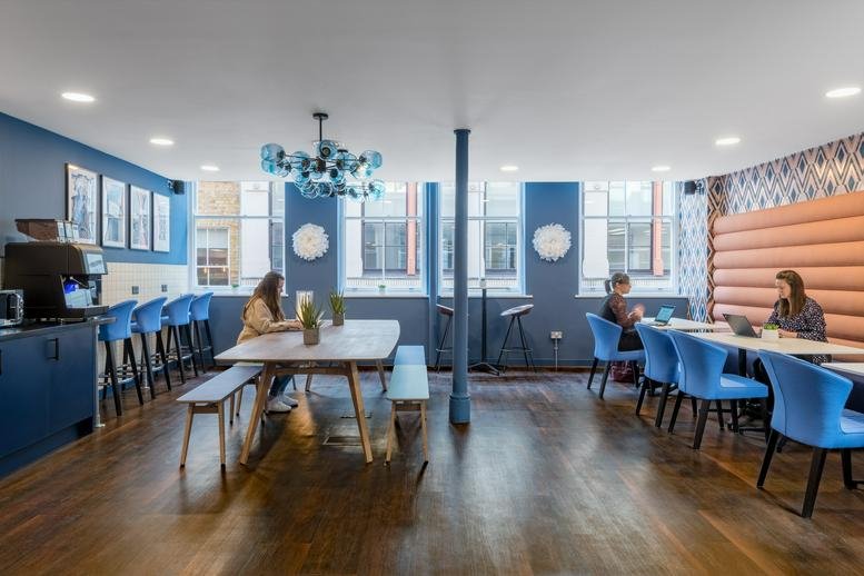Stylish breakout space with blue velvet chairs, wooden tables, and a blue glass chandelier.