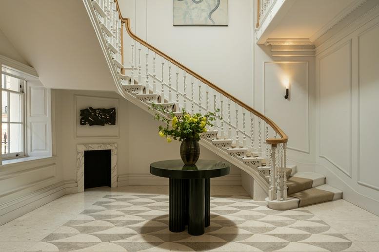 Elegant grand staircase at 75 Grosvenor Street with white spindles and a dark marble table.