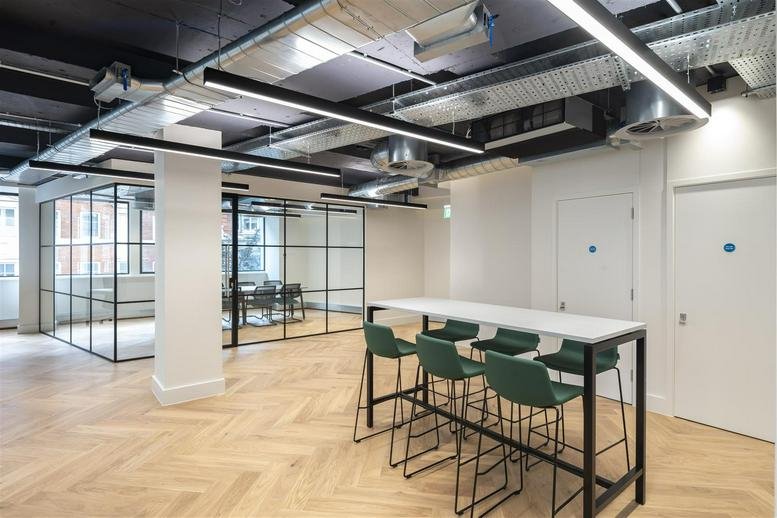 Communal breakout area featuring a white high table, green bar stools, and herringbone wood flooring.