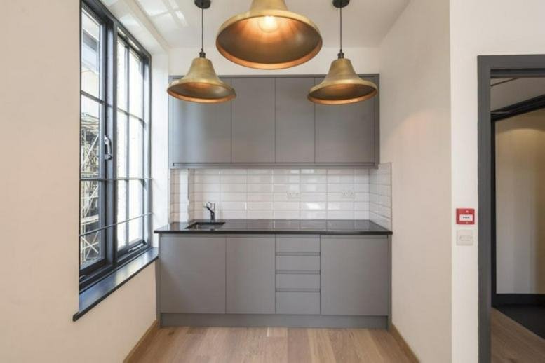 Modern kitchenette with grey cabinetry, white tiled backsplash, and brass pendant lights.