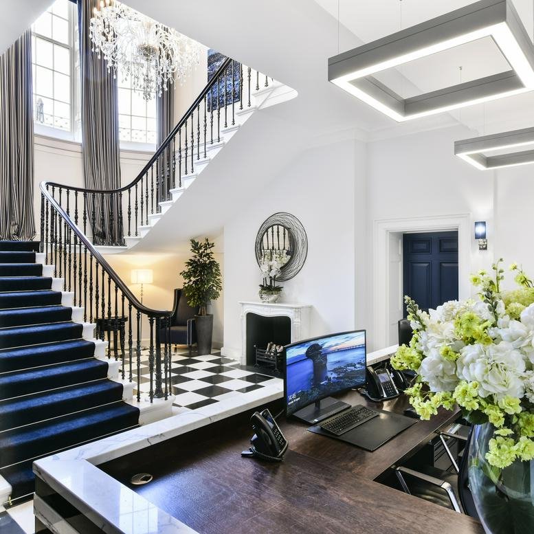 Bright reception area with a grand staircase, blue carpet, and checkered flooring.
