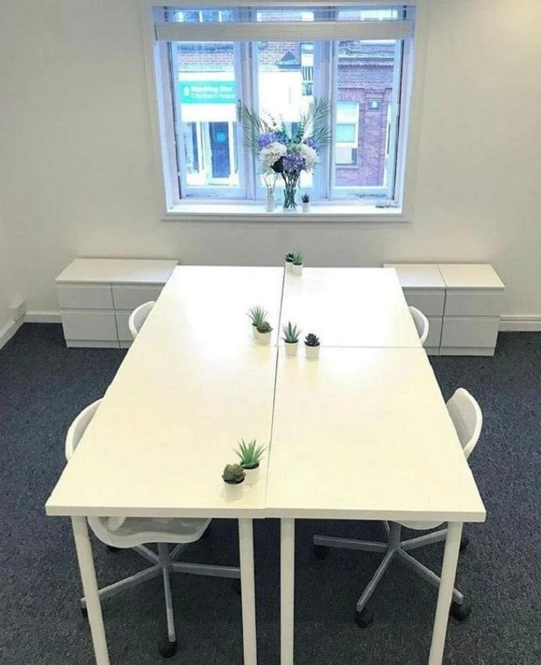 Bright coworking area with white desks, small potted succulents, and a large window.