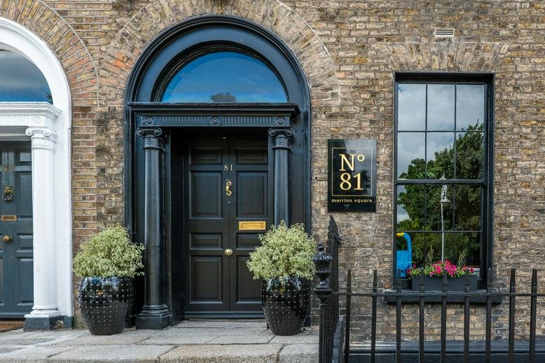Exterior of 81 Merrion Square, Dublin, featuring a classic brick facade and black arched doorway.