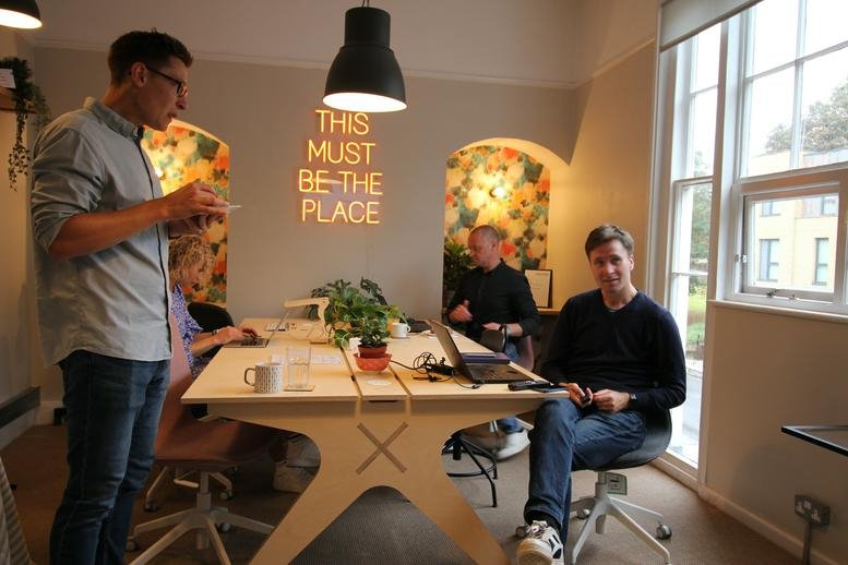 Modern workspace at 8a London Road, Tunbridge Wells, Kent with a neon sign and coworkers at a large desk.