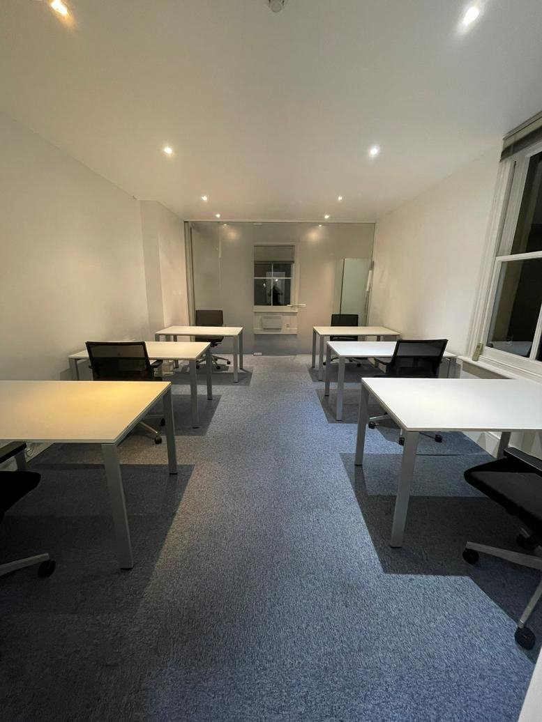 Modern open-plan office with white desks and black ergonomic chairs.