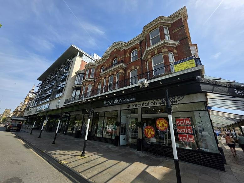 Street-level view of the building facade showing large windows and a covered walkway.