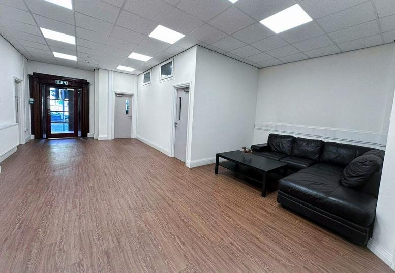 Spacious communal lounge featuring a black L-shaped sofa and warm wood-style flooring.