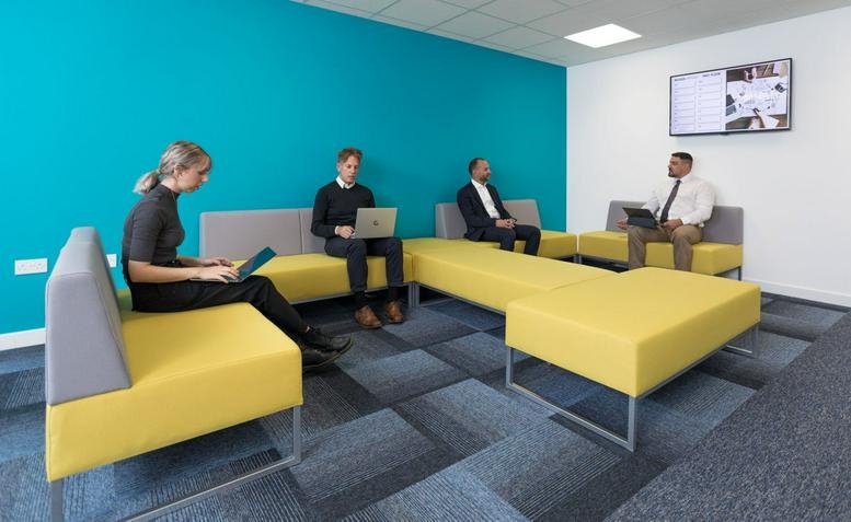 Spacious communal lounge at Access Business Centre featuring yellow modular seating and a vibrant teal wall.