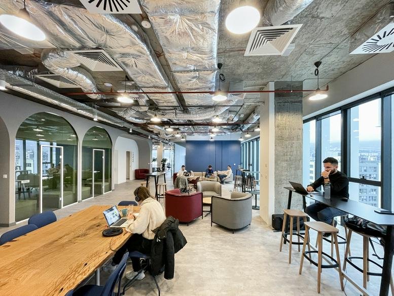Lively coworking lounge at Advance Business Center with industrial ceilings and natural wood tables.
