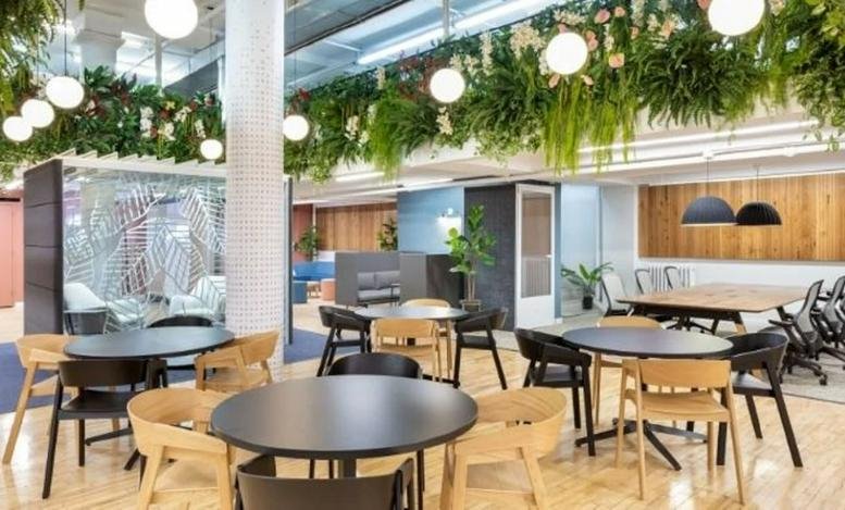 Spacious coworking area with black and wood dining tables under a ceiling of lush hanging greenery.