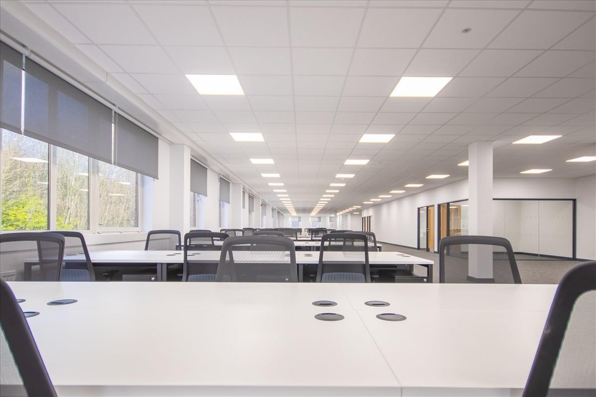 Spacious open-plan workspace at Amber Court, William Armstrong Drive with rows of white desks and overhead lighting.