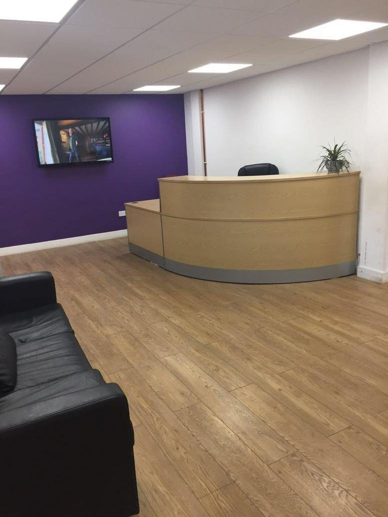 Modern reception area featuring a curved wood desk, purple feature wall, and wood-style flooring.