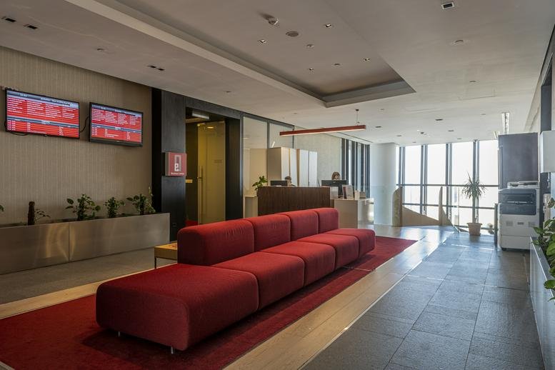 Spacious reception and lounge area at Next Level with a long red sofa and city views.