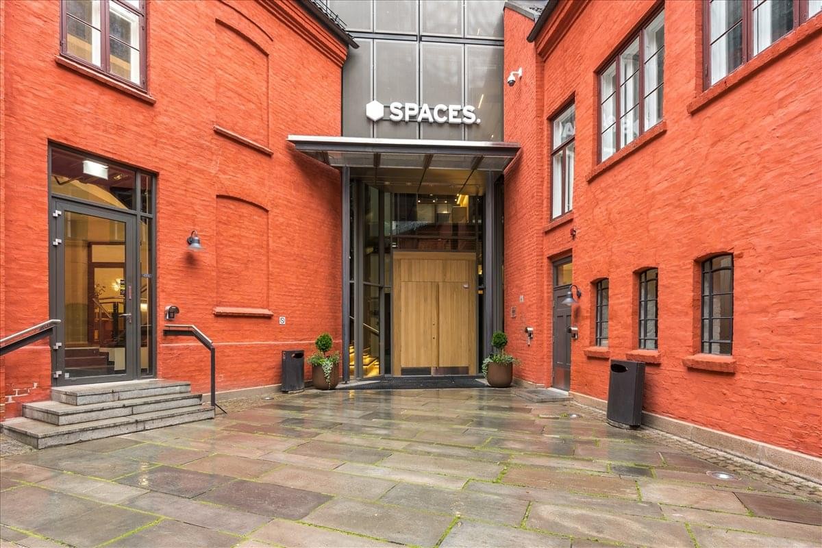 Exterior entrance of Apotekergata 10 featuring red brick walls and a glass doorway under a Spaces sign.