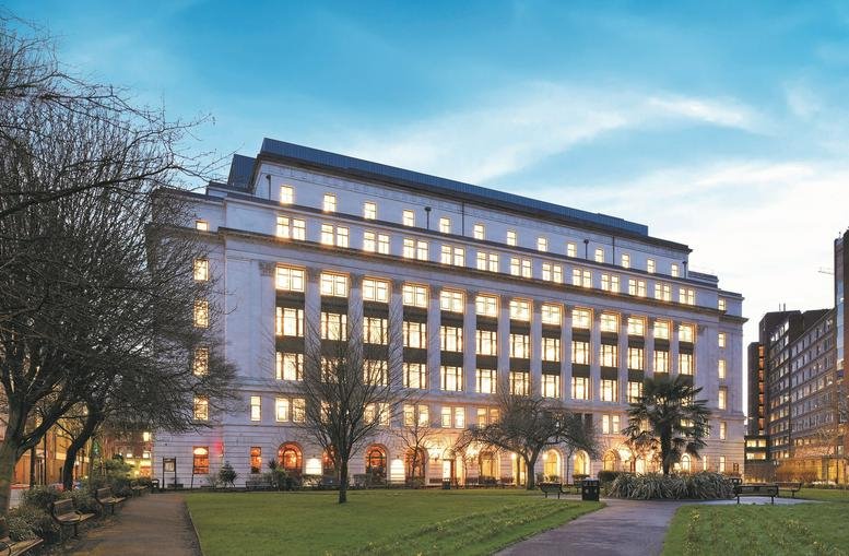 Exterior view of the illuminated facade of Arkwright House at dusk with a green park in front.
