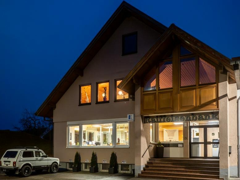 Exterior view of the Alte Bank Biberach building entrance lit up at dusk.