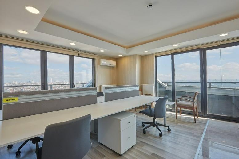 Bright open-plan office area with wood-style flooring and expansive city views through floor-to-ceiling windows.