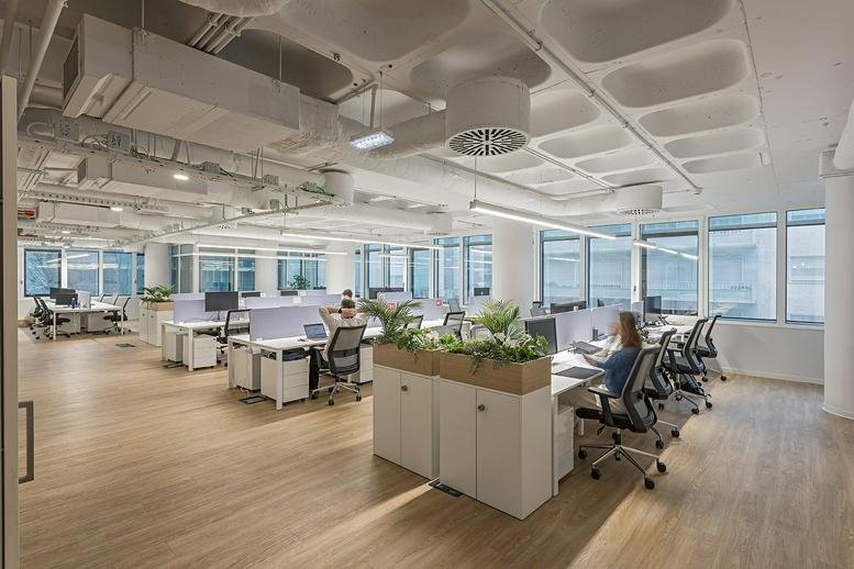 Spacious open office with clusters of white desks and green planter dividers.