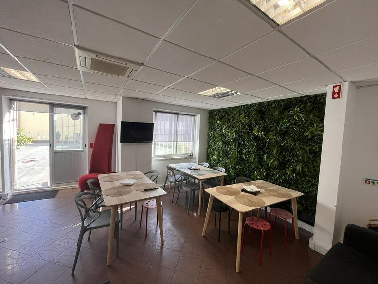 Spacious communal dining area with modern tables, red seating, and a lush green feature wall at Avenida António Augusto de Aguiar 24.