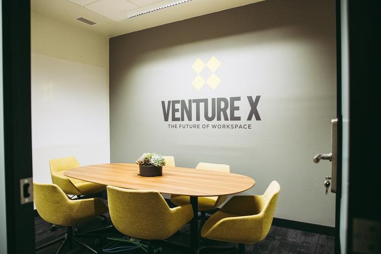 Sunlit meeting room with yellow chairs, an oval table, and glass entry doors.