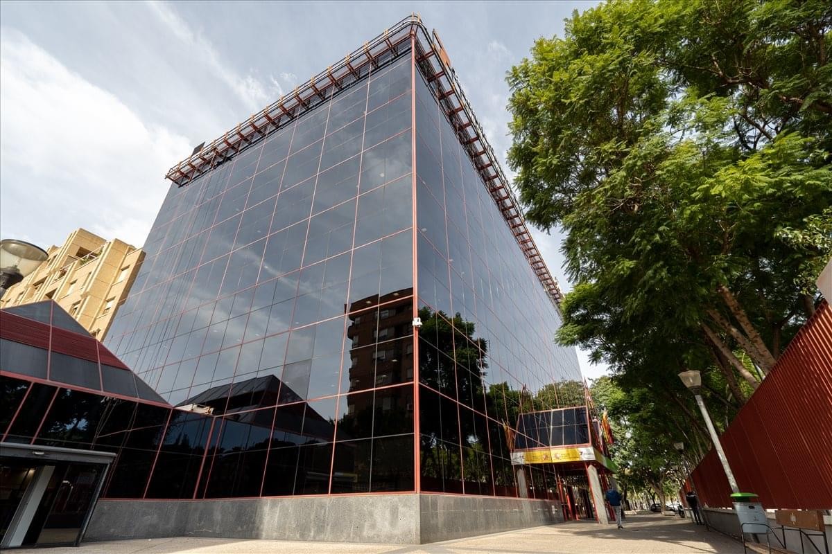 Modern glass-facade exterior of the Avenida de los Pinos 7 office building with surrounding greenery.