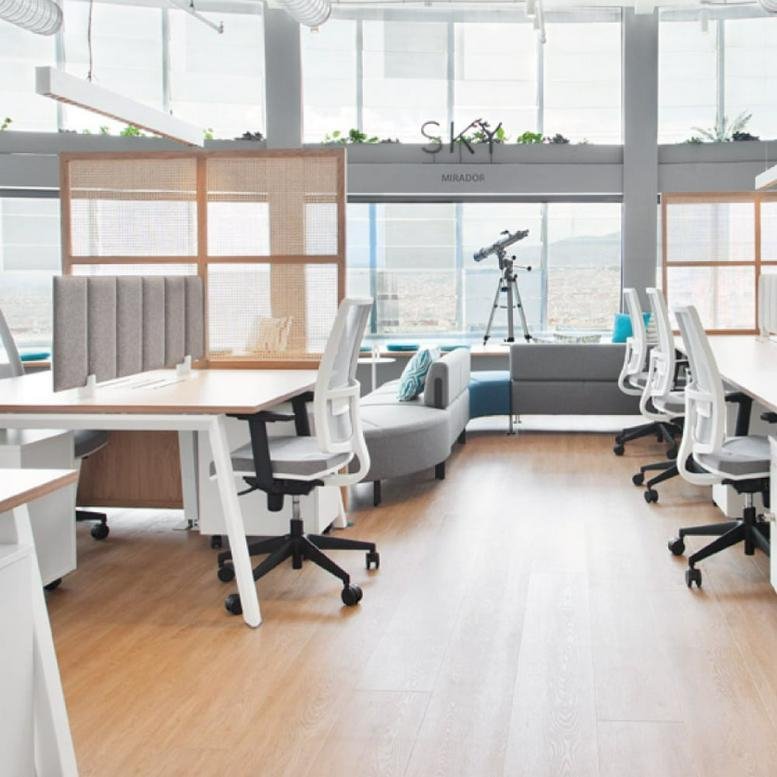 Open-plan workspace at Torre Glòries with white ergonomic desks, chairs, and floor-to-ceiling windows.
