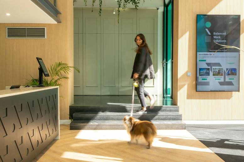 Spacious reception lobby at Avenida Duque de Loulé 110 featuring wood floors and a person walking a dog.