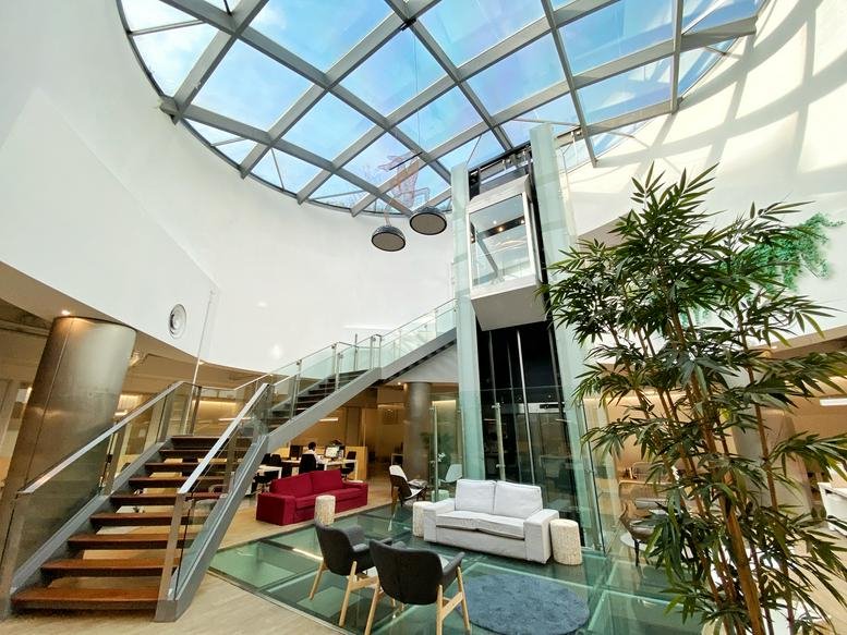 Spacious communal lounge with a glass-walled elevator, modern seating, and a large indoor tree.