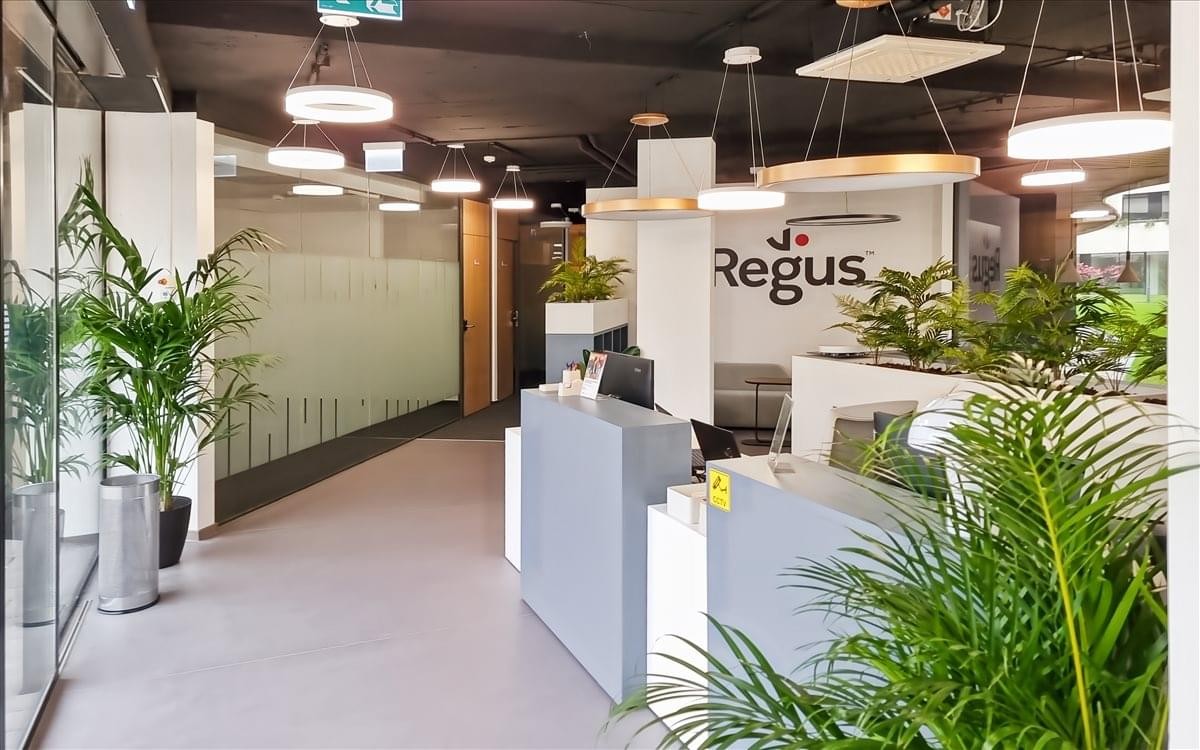 Reception area at Cédrus Offices with a grey front desk, indoor palms, and modern pendant lighting.