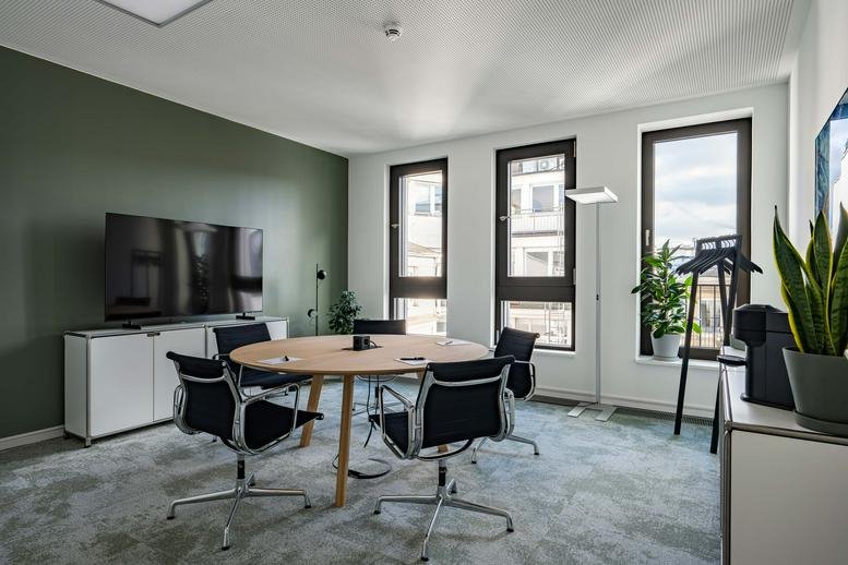 Meeting room at Ballindamm 3 featuring a round wooden table, black chairs, and a green feature wall.