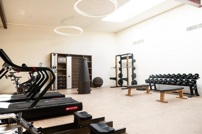 Bright fitness center featuring treadmills, weight racks, and modern ring lighting.