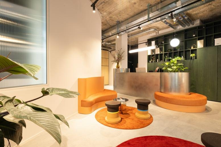 Bright reception area with a sleek metallic front desk, orange seating, and green cabinetry.
