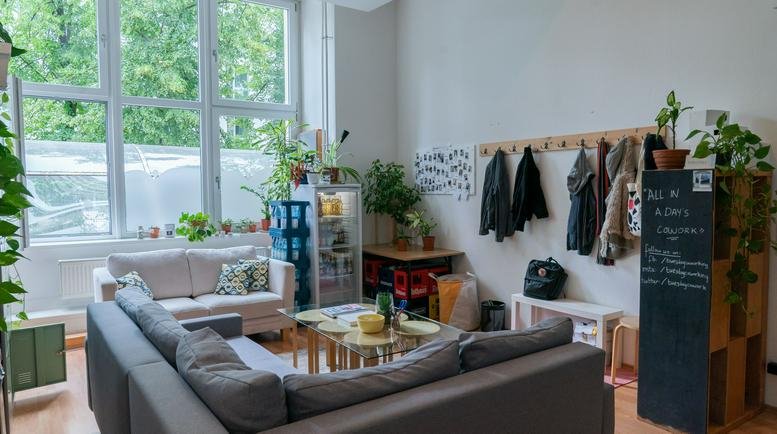 Spacious communal lounge with grey sofas, large windows, and many indoor plants at Belziger Strasse 69-71.