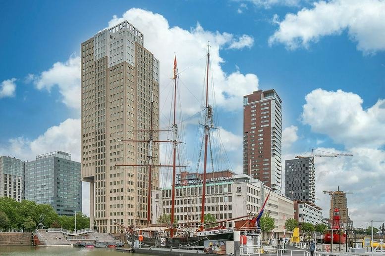 Exterior view of the tall concrete building alongside a harbor with sailing ships.