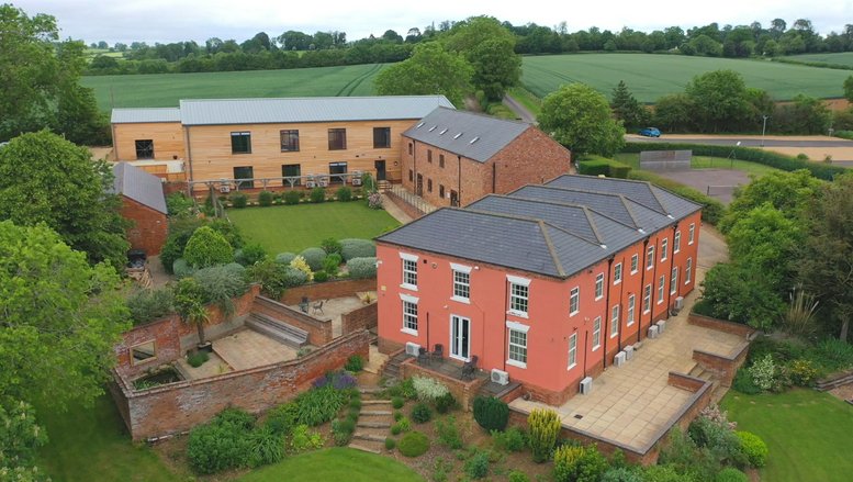 Aerial view of the red brick main building surrounded by lush green gardens and countryside.