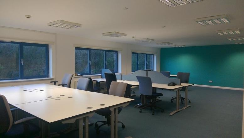 Spacious open-plan office with multiple desks and a teal feature wall.