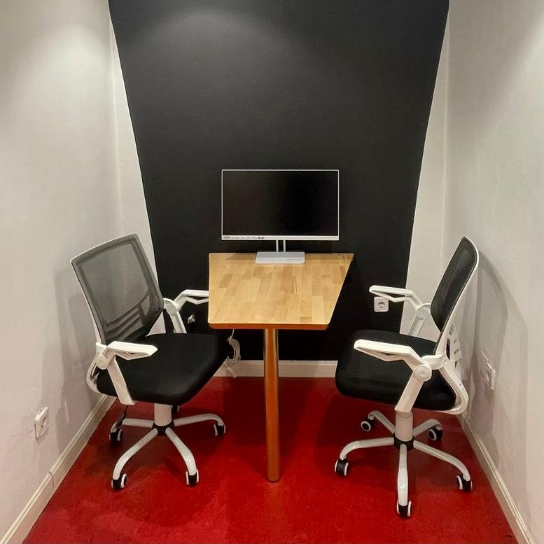 Compact two-person meeting space with a wooden table and black feature wall.