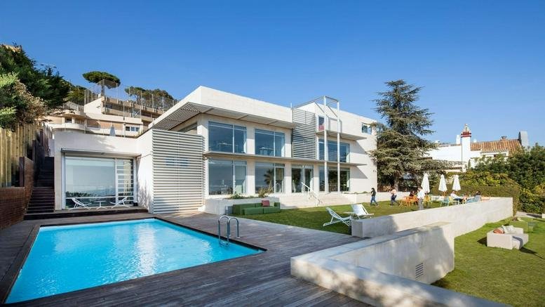 Exterior view of the white modern villa at Carrer de Lluís Muntadas 8, Barcelona with a swimming pool and lawn.