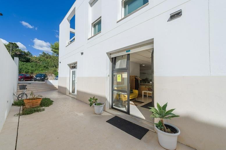 Modern white building exterior at Carrer de s’Illa Plana 5 with a glass entrance and potted plants.